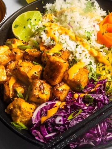 Sticky tofu bowl (AKA crispy tofu rice bowl) in a black bowl.