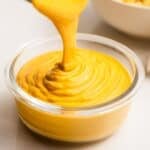 Vegan cheese sauce pouring into a glass bowl.