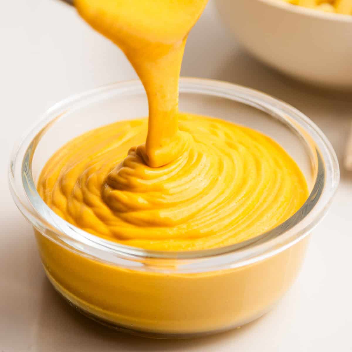 Vegan cheese sauce pouring into a glass bowl.