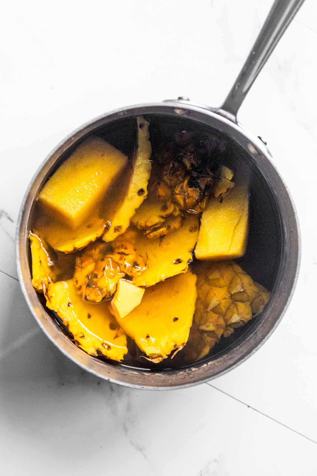 Water pouring into a pan with pineapple skins and a pineapple core.