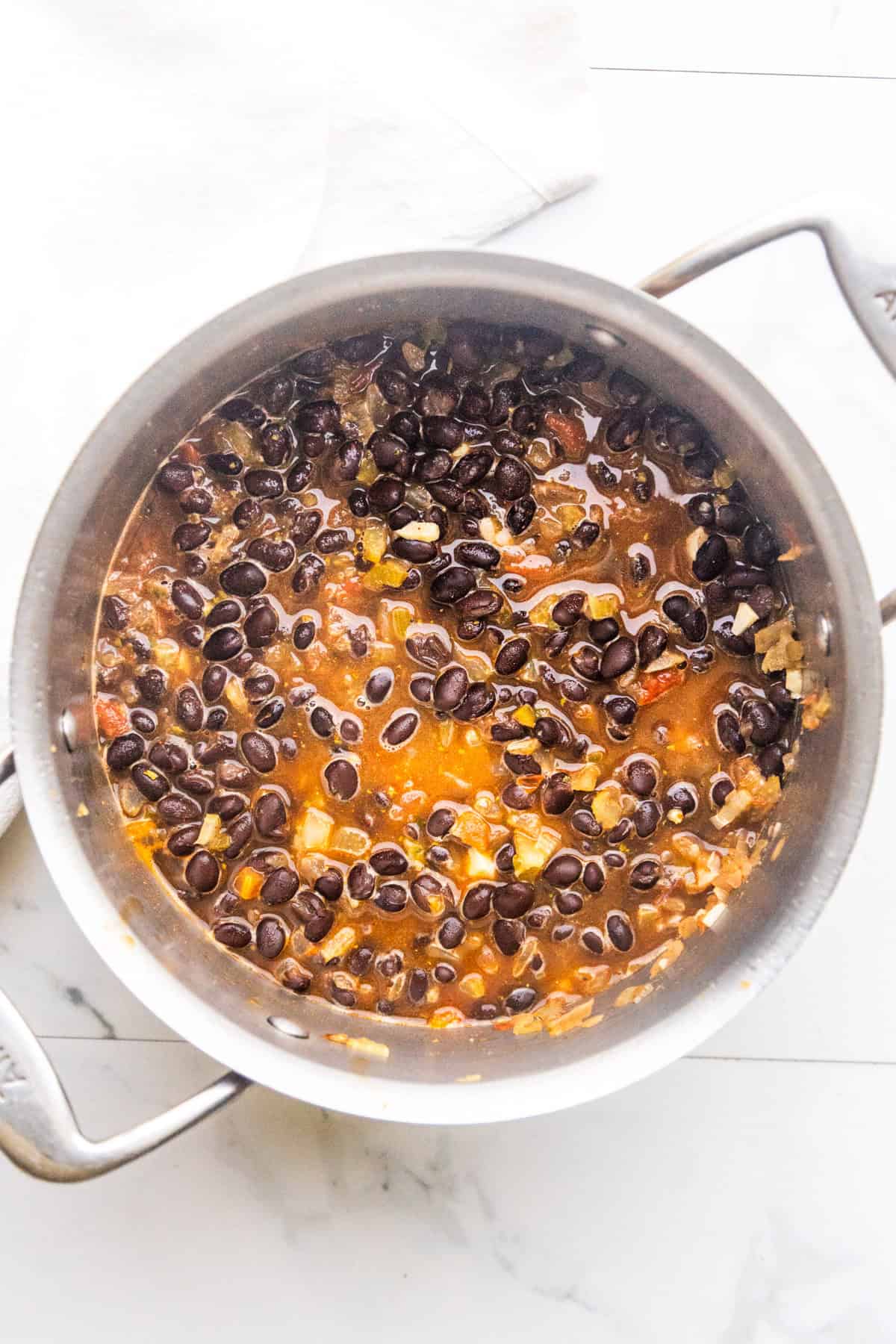 Veggies, water, and canned black beans sautéing in a pan.