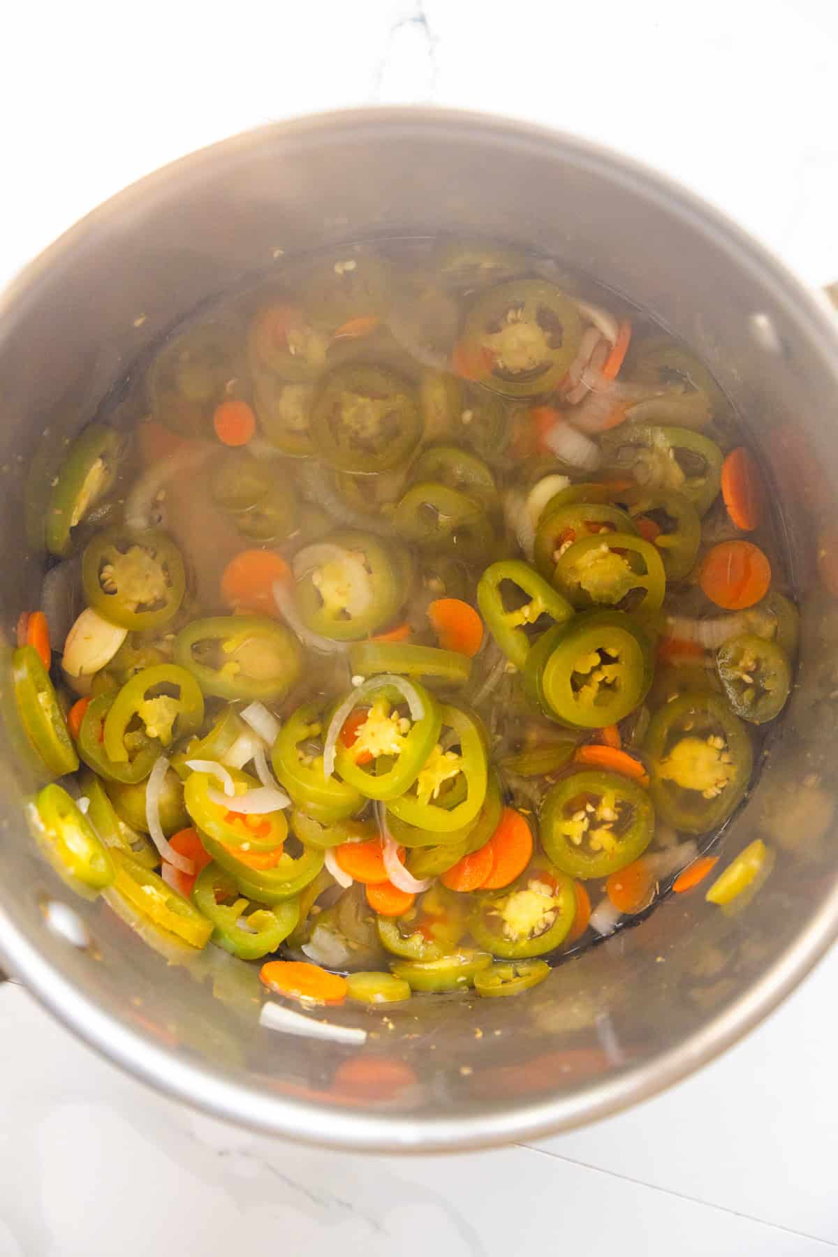 Jalapeños carrots and onions sautéing in a pan.