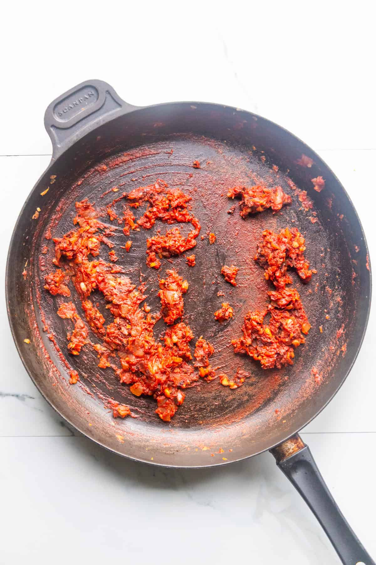 Onions and garlic with tomato paste sautéing in a skillet.