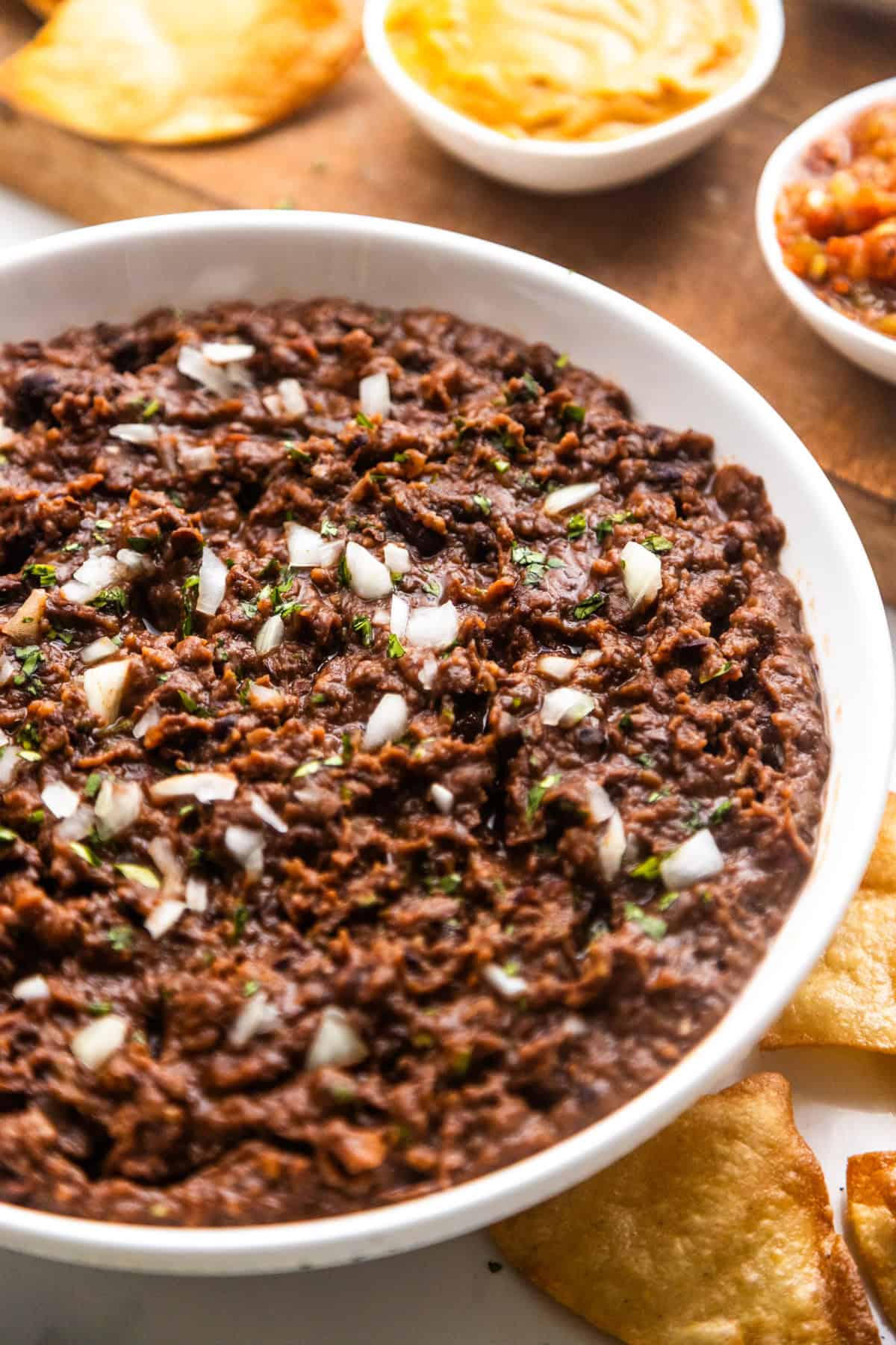 Vegan refried black beans from canned beans topped with onion and cilantro with salsa and chips on the side.