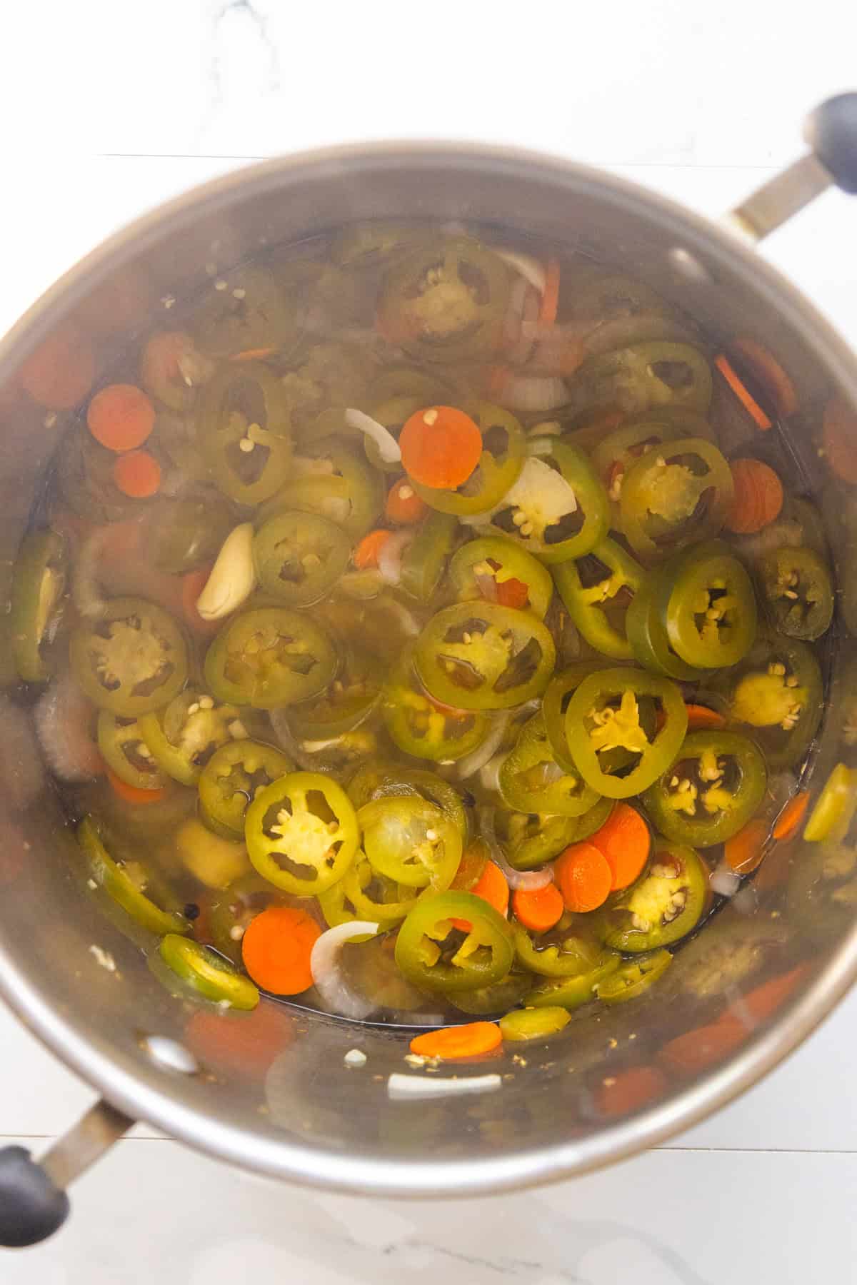Sautéed jalapeños carrots and onions in a pan with seasonings.