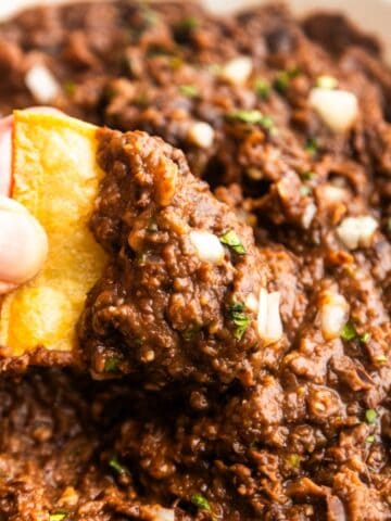 Chip dipping into vegan refried black beans with canned beans.
