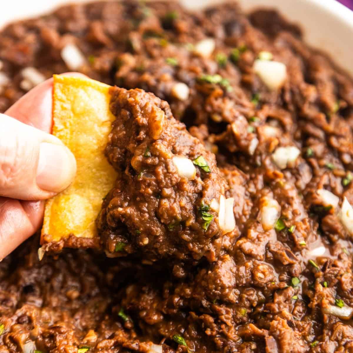 Chip dipping into vegan refried black beans with canned beans.