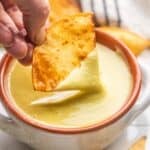 A chip dipping into a bowl of creamy jalapeño sauce.