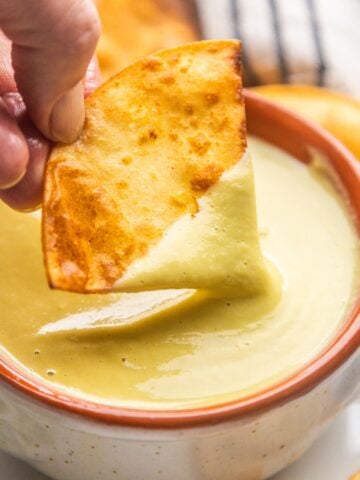 A chip dipping into a bowl of creamy jalapeño sauce.