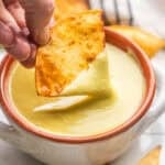 A chip dipping into creamy jalapeño sauce in a bowl.