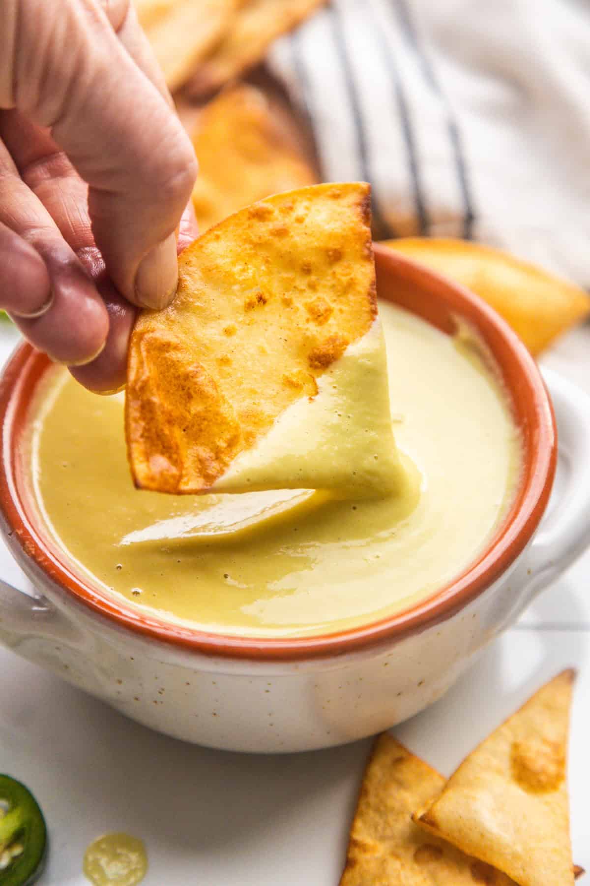 A chip dipping into creamy jalapeño sauce in a bowl.