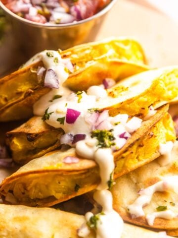 Crispy potato tacos topped with vegan lime crema, chopped red onions, and fresh cilantro.