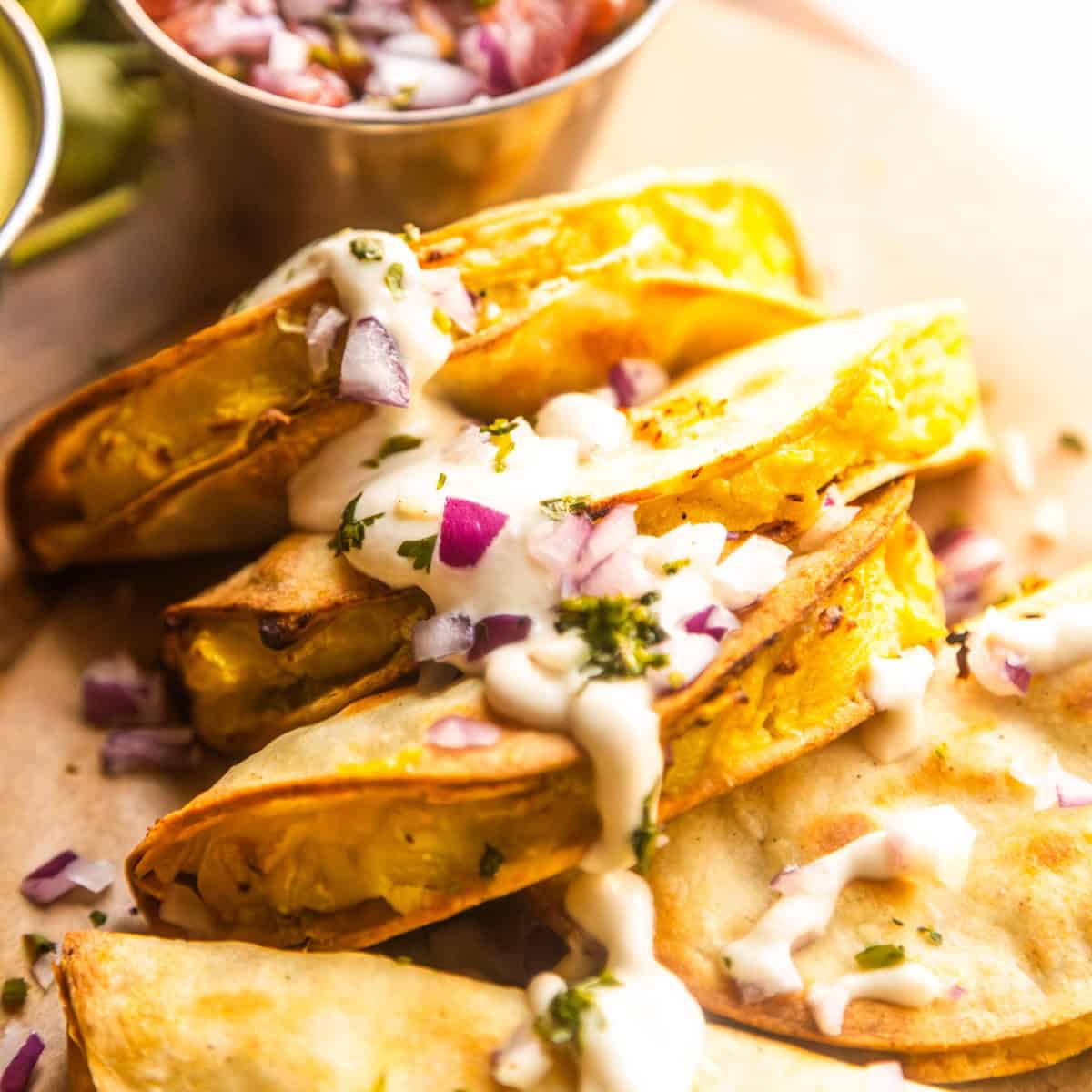 Crispy potato tacos topped with vegan lime crema, chopped red onions, and fresh cilantro.