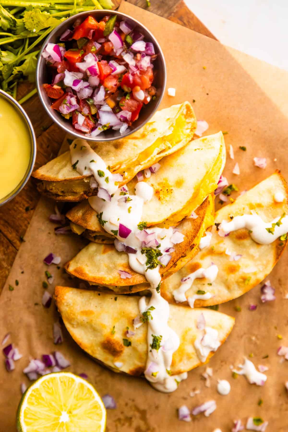 Crispy potato tacos on a wooden board topped with lime crema, chopped red onions, & fresh parsley.