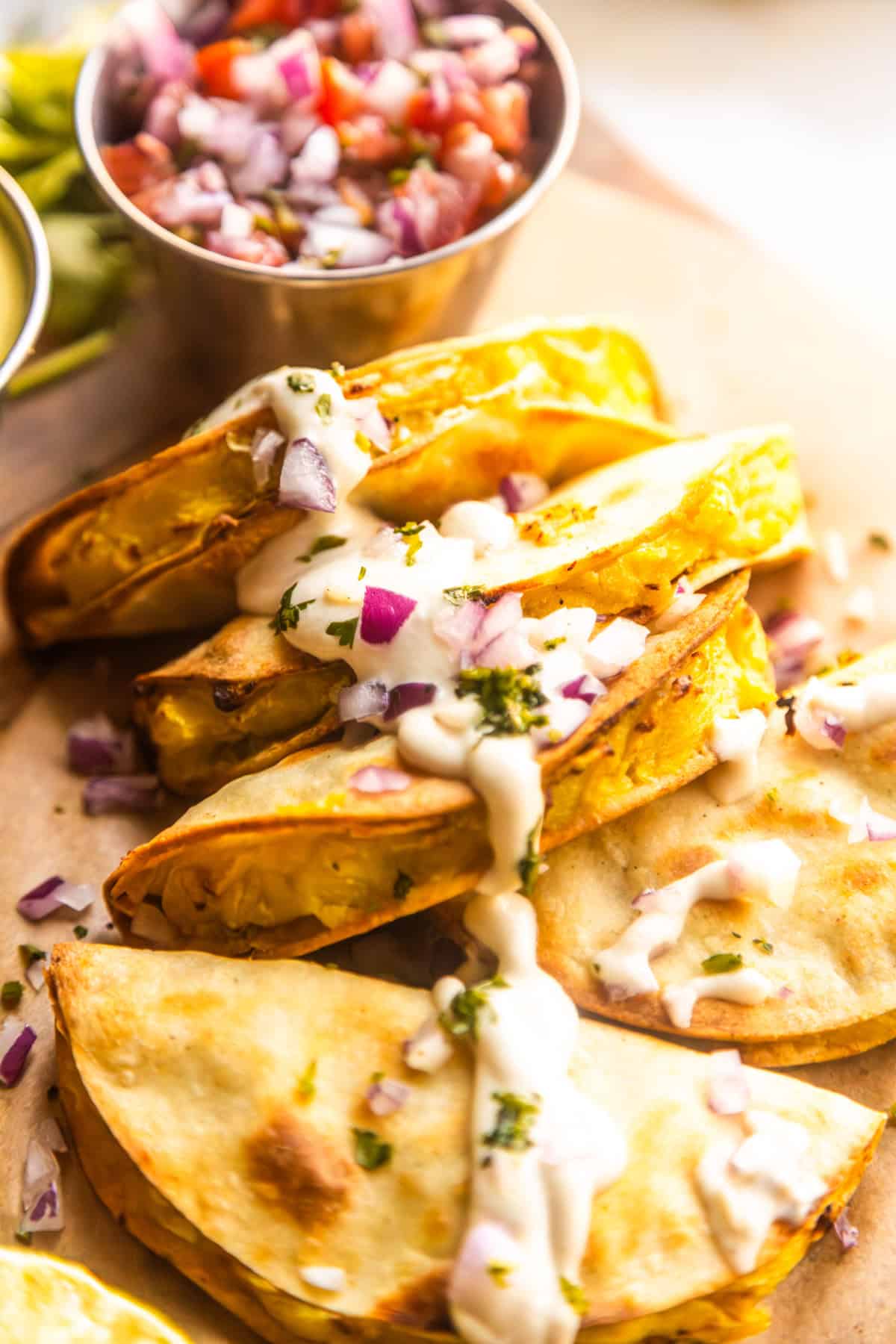 Crispy potato tacos topped with vegan lime crema, chopped red onions, and chopped fresh cilantro.