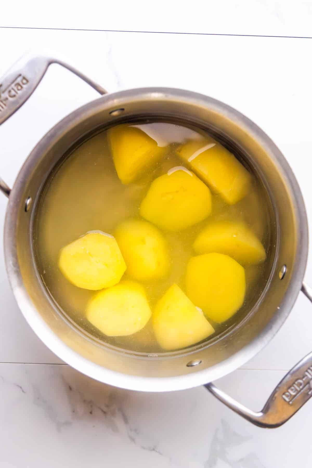 Peeled Yukon Gold potatoes cooking in a pot with boiling water.