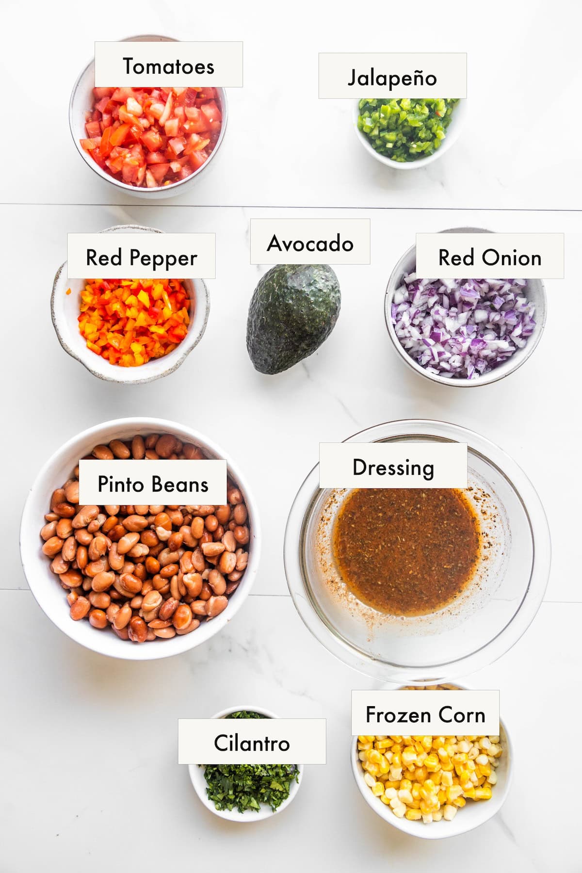 All ingredients for pinto bean corn salad in labeled bowls on a counter.