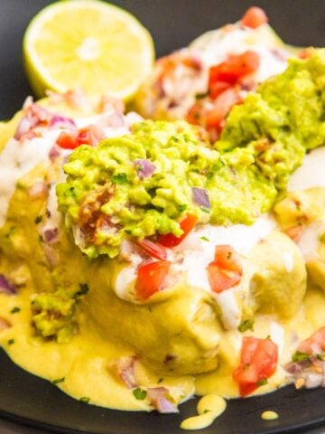 Vegan bean and rice wet burritos in a bowl topped with fresh guacamole and pico de Gallo.