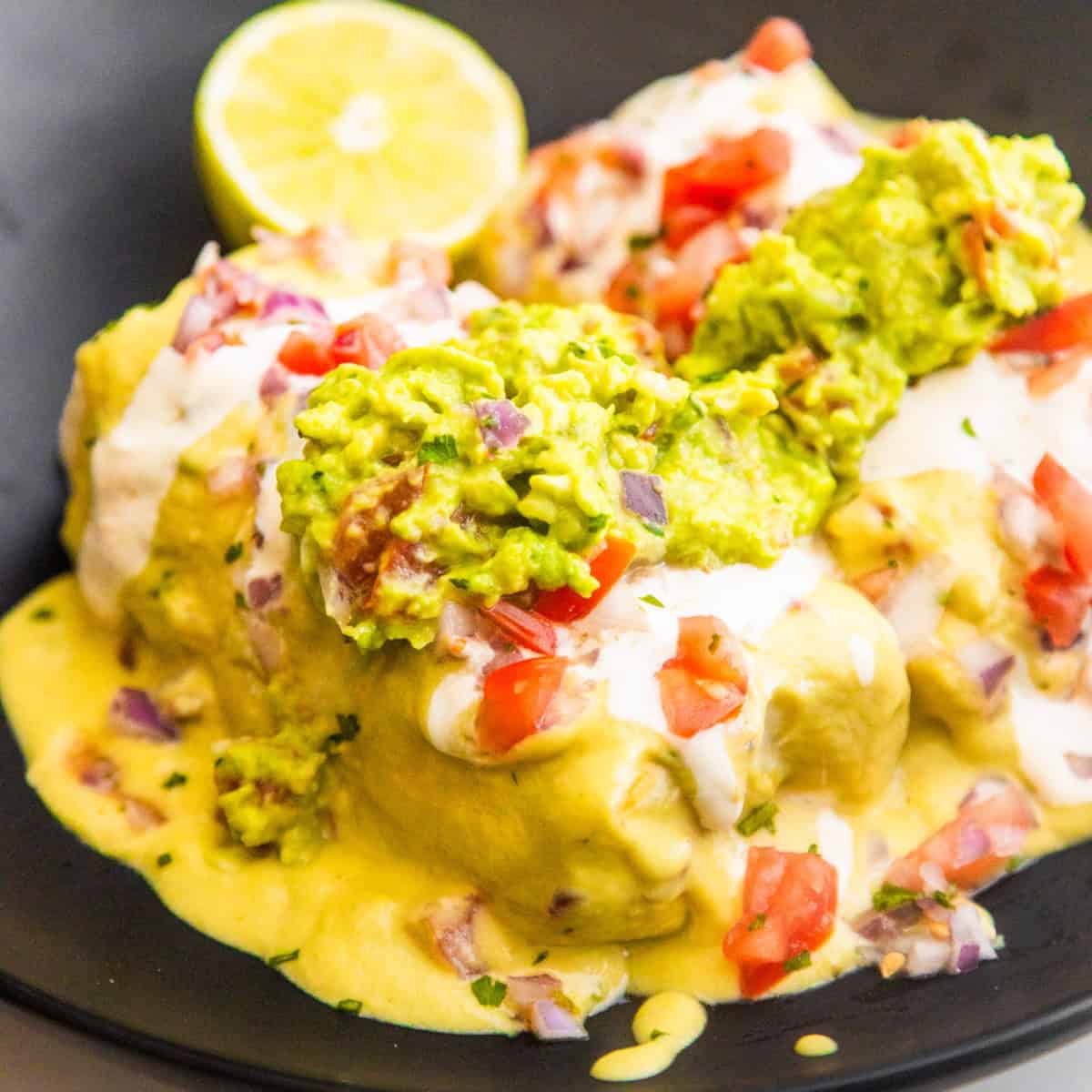 Vegan bean and rice wet burritos in a bowl topped with fresh guacamole and pico de Gallo.