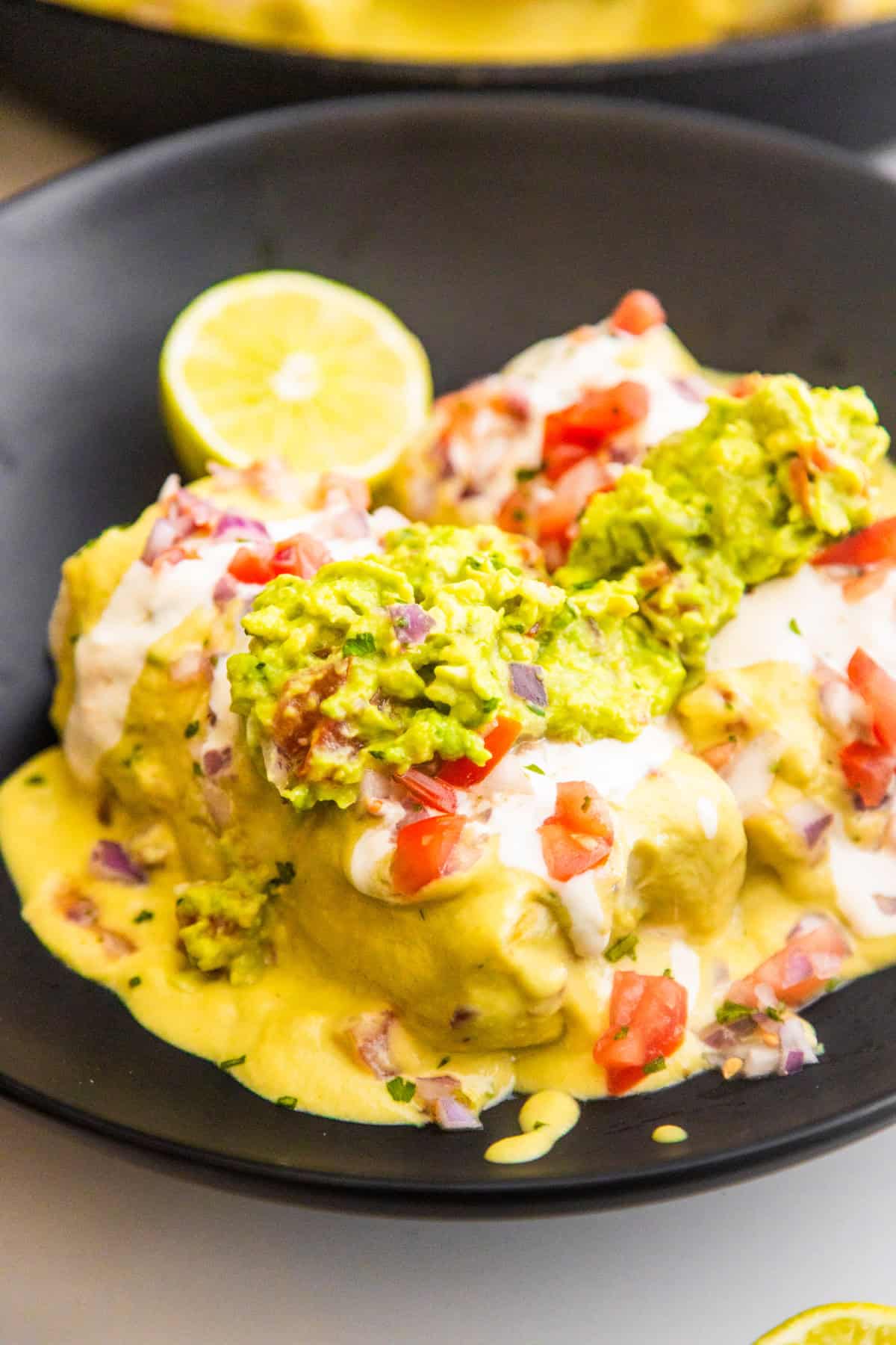 Vegan smothered bean and rice wet burritos in a bowl topped with fresh guacamole and pico de Gallo.