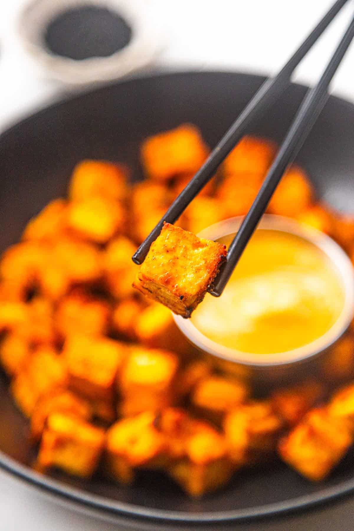 Close up of chopsticks holding a crispy sweet and spicy maple sriracha tofu.