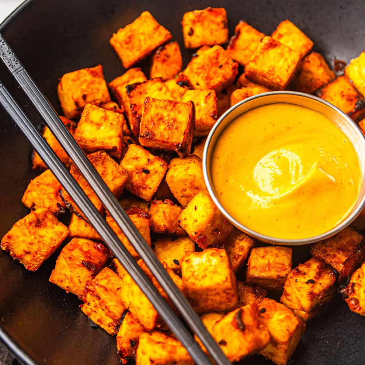 Air fryer sweet and spicy maple sriracha tofu in a bowl with sauce on the side.