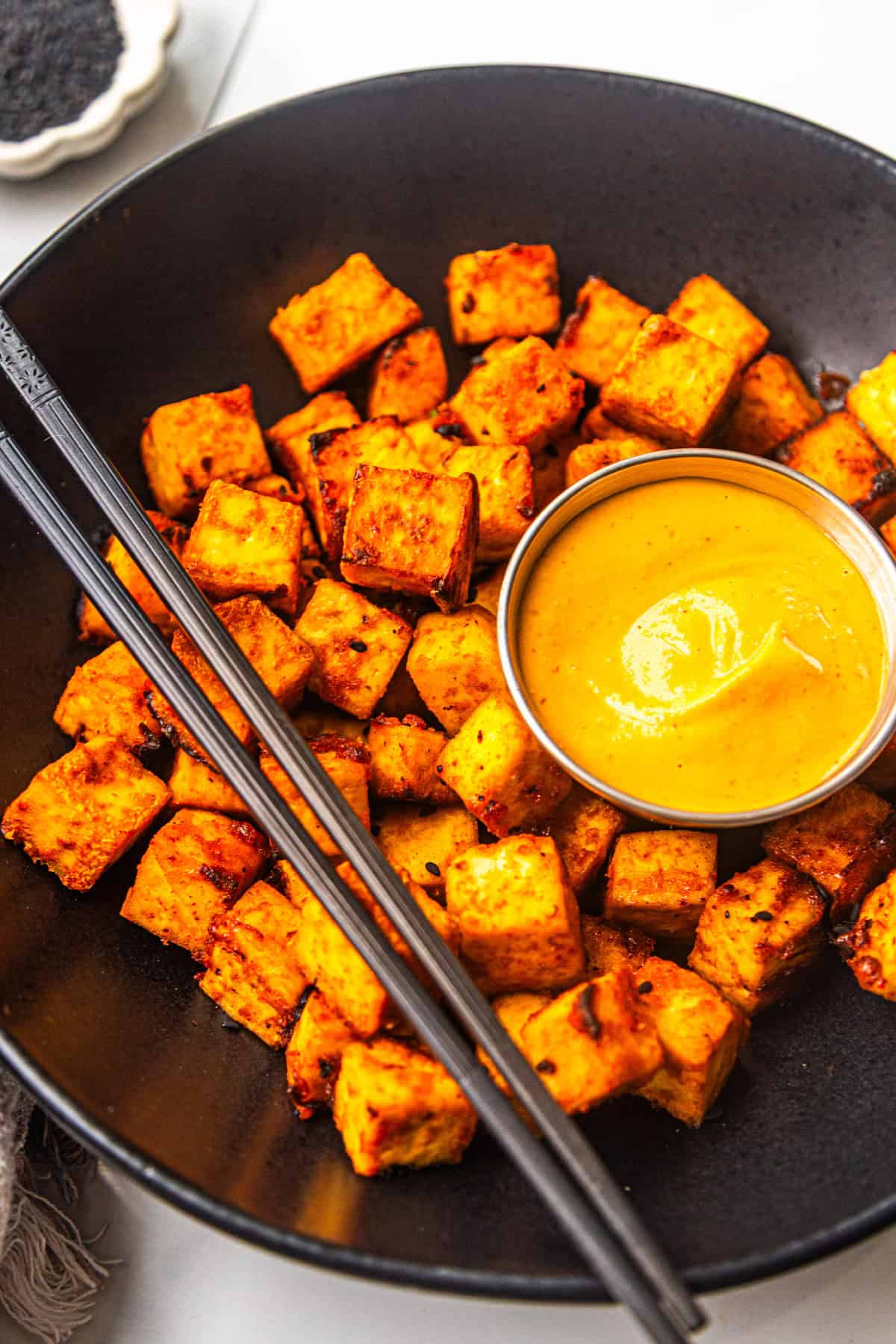 Air fryer sweet and spicy maple sriracha tofu in a bowl with sauce on the side.