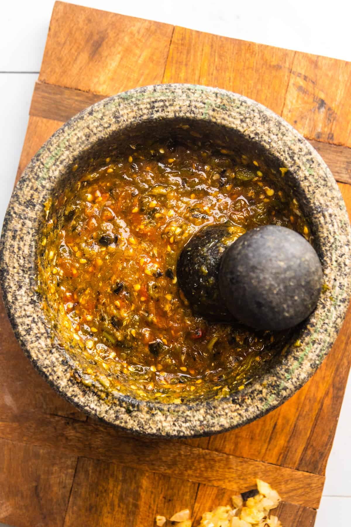Crushed fresh green chilis, garlic, and tomatoes in a molcajete.