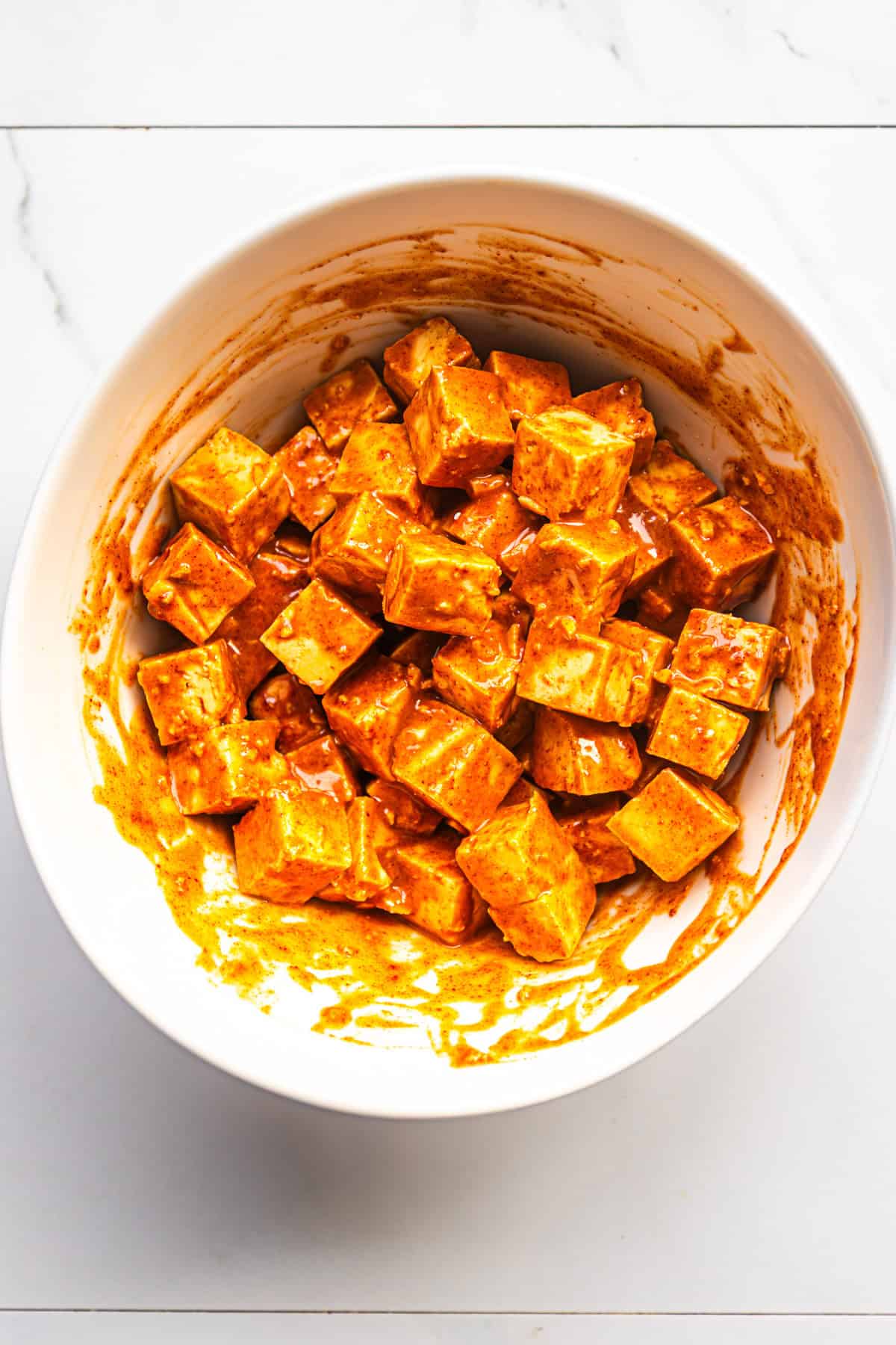 Sweet and spicy maple sriracha tofu in a bowl mixing with glaze.