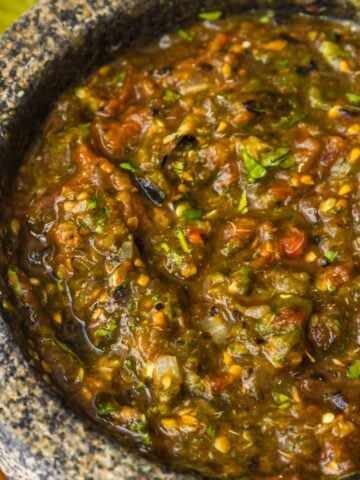 Molcajete salsa in a large molcajete with tortilla chips, lime wedges, and cilantro on the side.