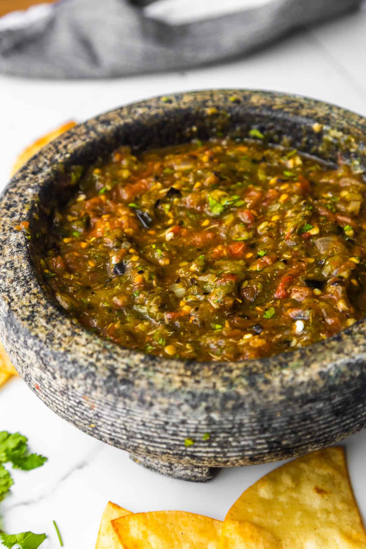 Homemade salsa in a molcajete with chips and cilantro on the side.