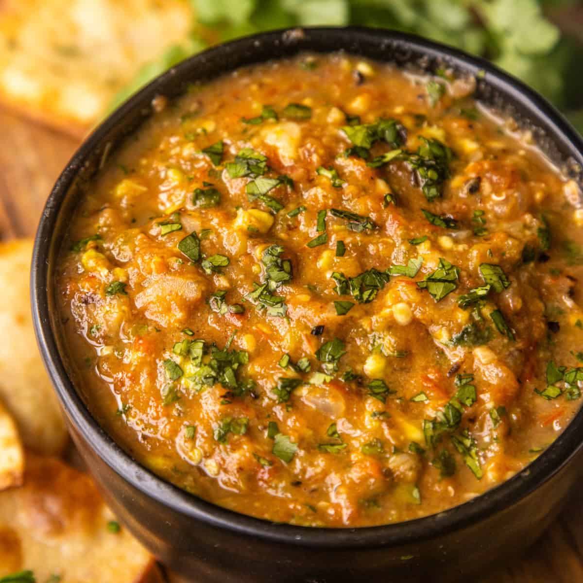 Roasted charred tomato salsa in a bowl with chips and cilantro on the side.