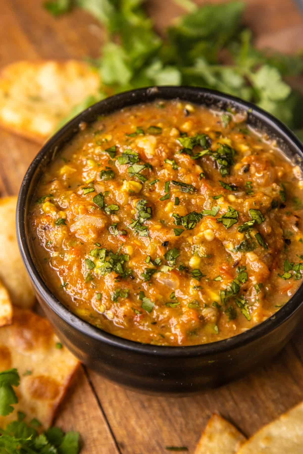 Roasted charred tomato salsa in a bowl with chips and cilantro on the side.