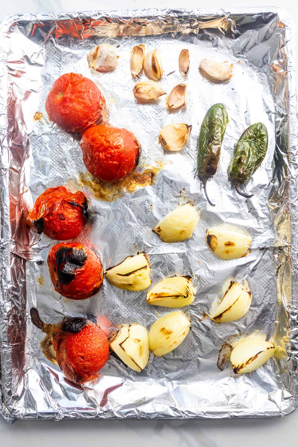 Roasted tomatoes, jalapeños, garlic, and onions on a cookie sheet.