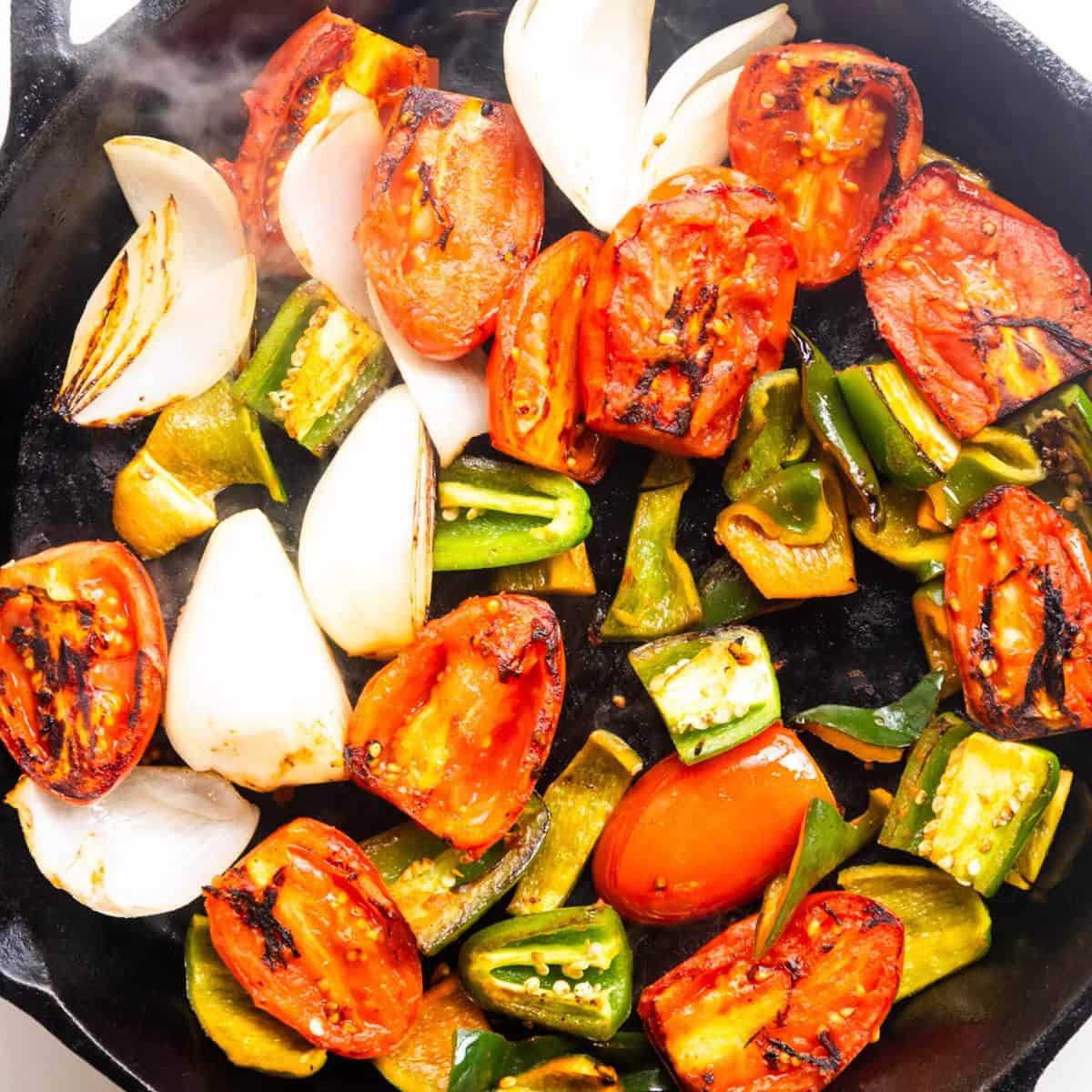 Veggies charring in a cast iron pan.