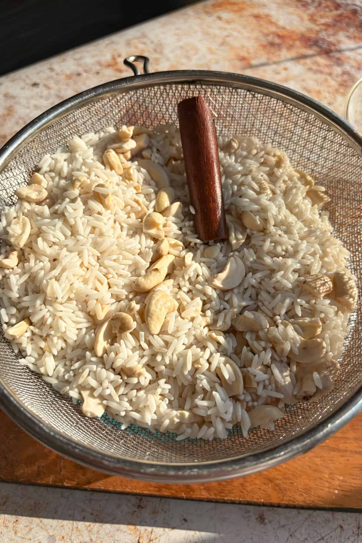 Soaked rice, cashews, and cinnamon in a strainer.