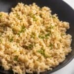 Homemade brown rice in a bowl with a wooden spoon on the side.