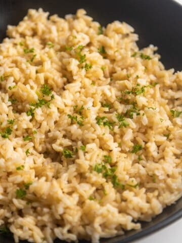 Homemade brown rice in a bowl with a wooden spoon on the side.