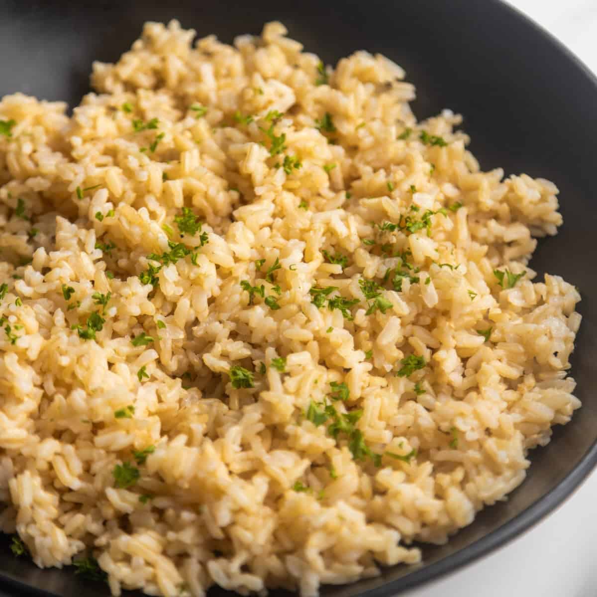 Homemade brown rice in a bowl with a wooden spoon on the side.