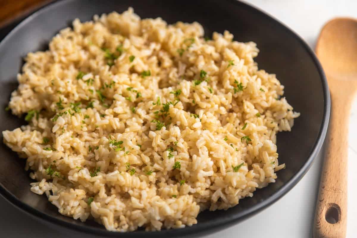 Brown rice in a black bowl topped with chopped parsley.