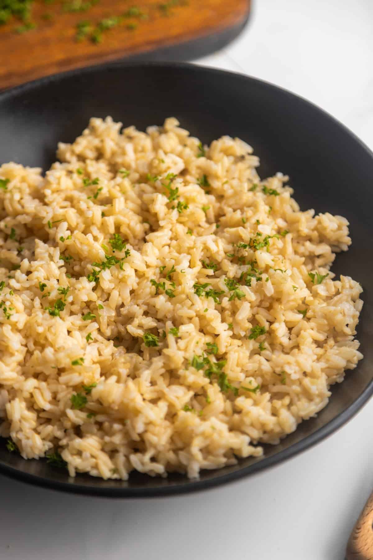 Homemade brown rice in a black bowl with a wooden spoon on the side.