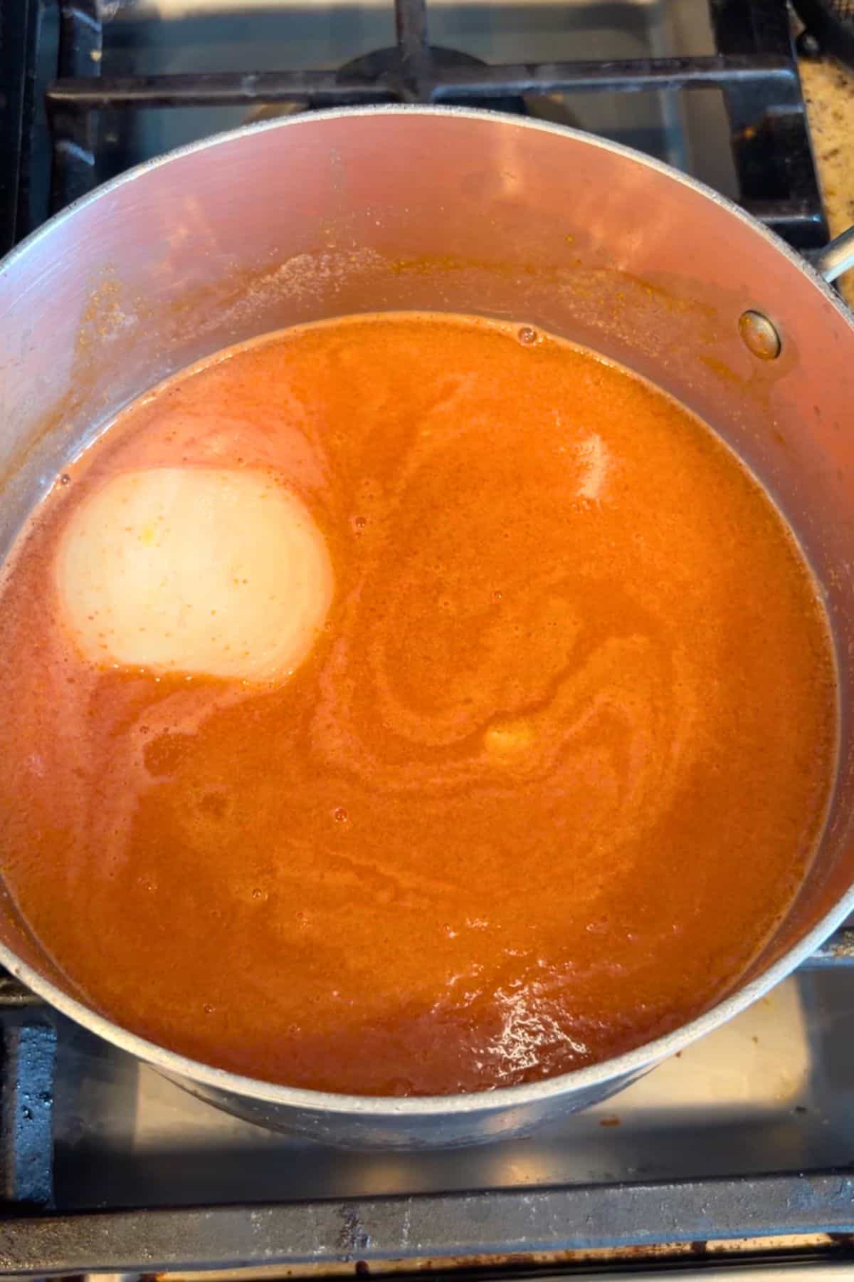 Toasted rice in a pan with tomato broth, veggies, and spices.