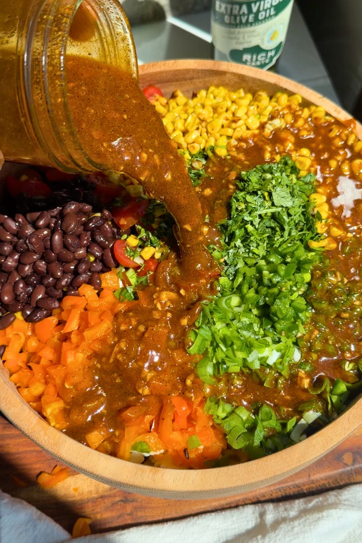 Chili lime vinaigrette pouring into a salad bowl with chopped veggies.