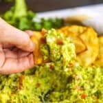 Chip dipping into a bowl with guacamole and chips on the side.