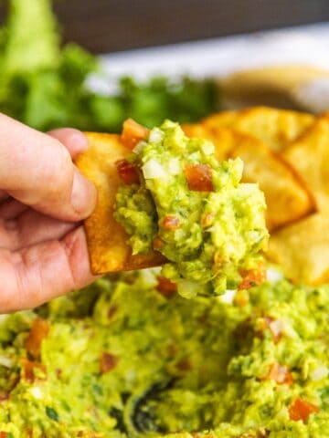 Chip dipping into a bowl with guacamole and chips on the side.