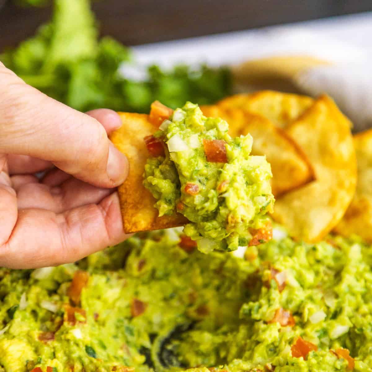 Chip dipping into a bowl with guacamole and chips on the side.