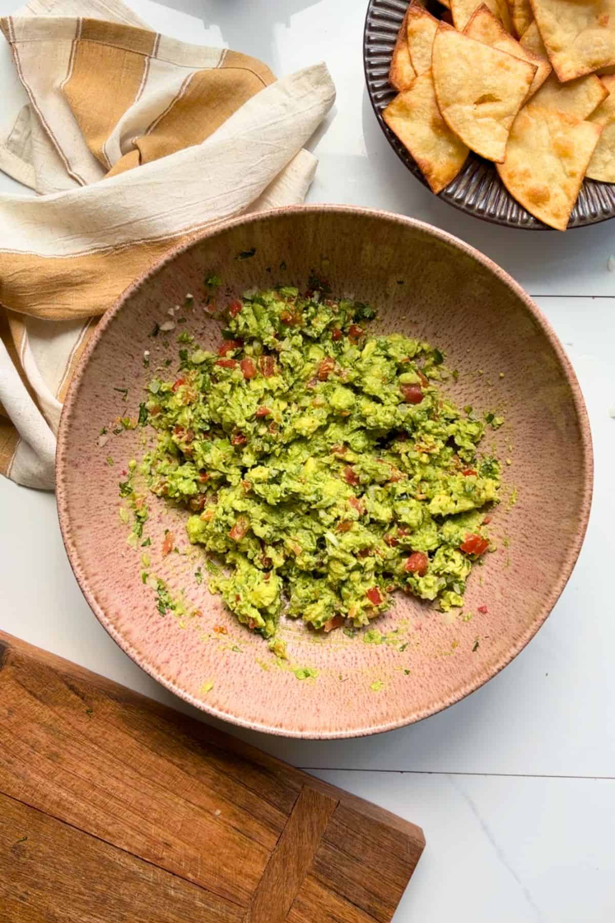 Finished guacamole in a bowl with chips on the side.