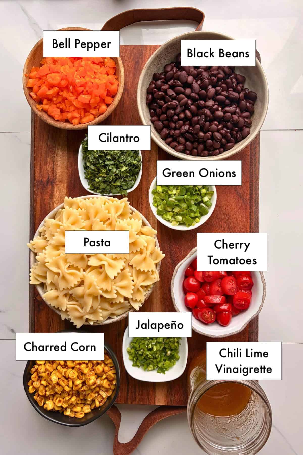 All ingredients needed to make southwest pasta salad in bowls on a table.