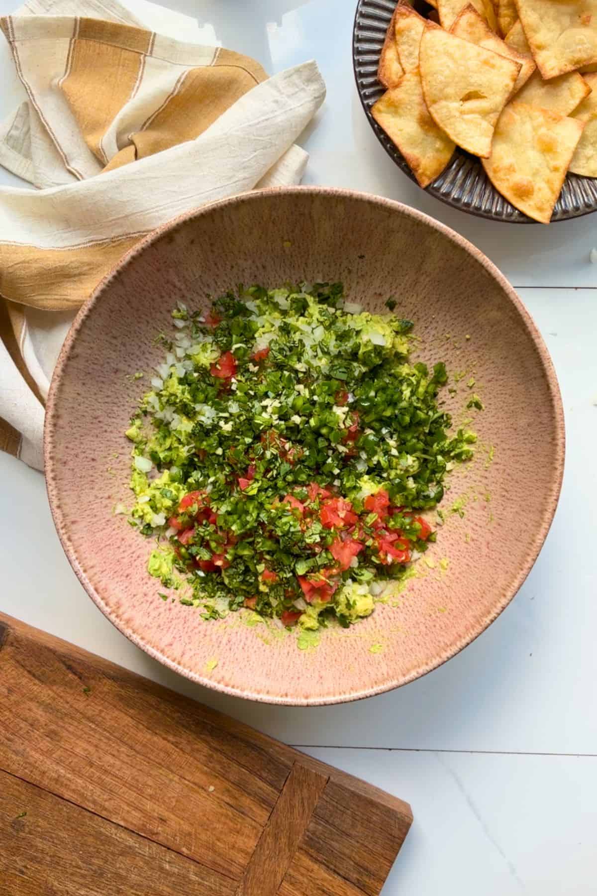 Mashed avocado with chopped veggies mixing in.