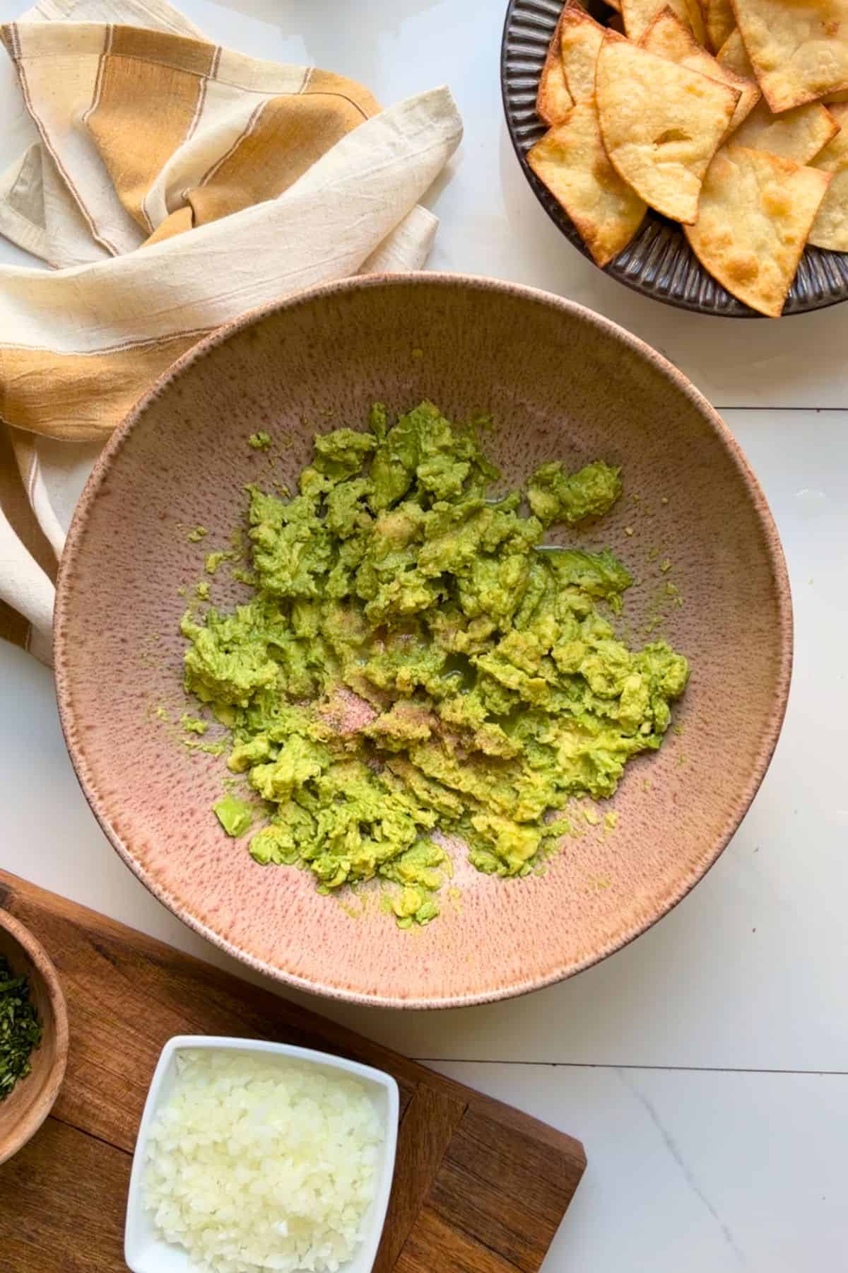 Mashed avocado in a bowl with salt and lime juice mixing in.